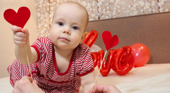 Baby looking at camera wearing red and holding paper heart cutouts. 