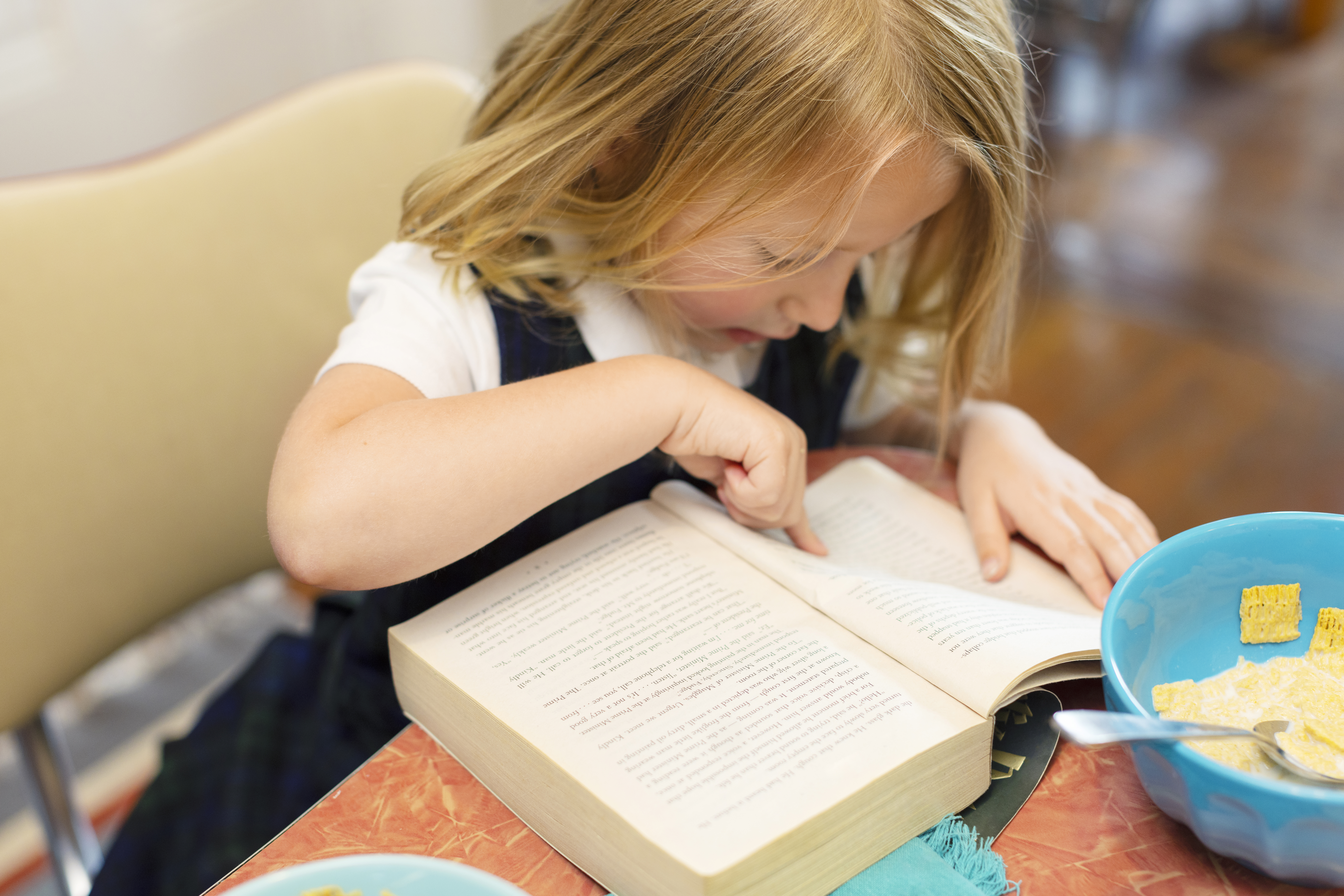 A little girl with blonde hair pointing her finger into a book, preparing for first day of school. 