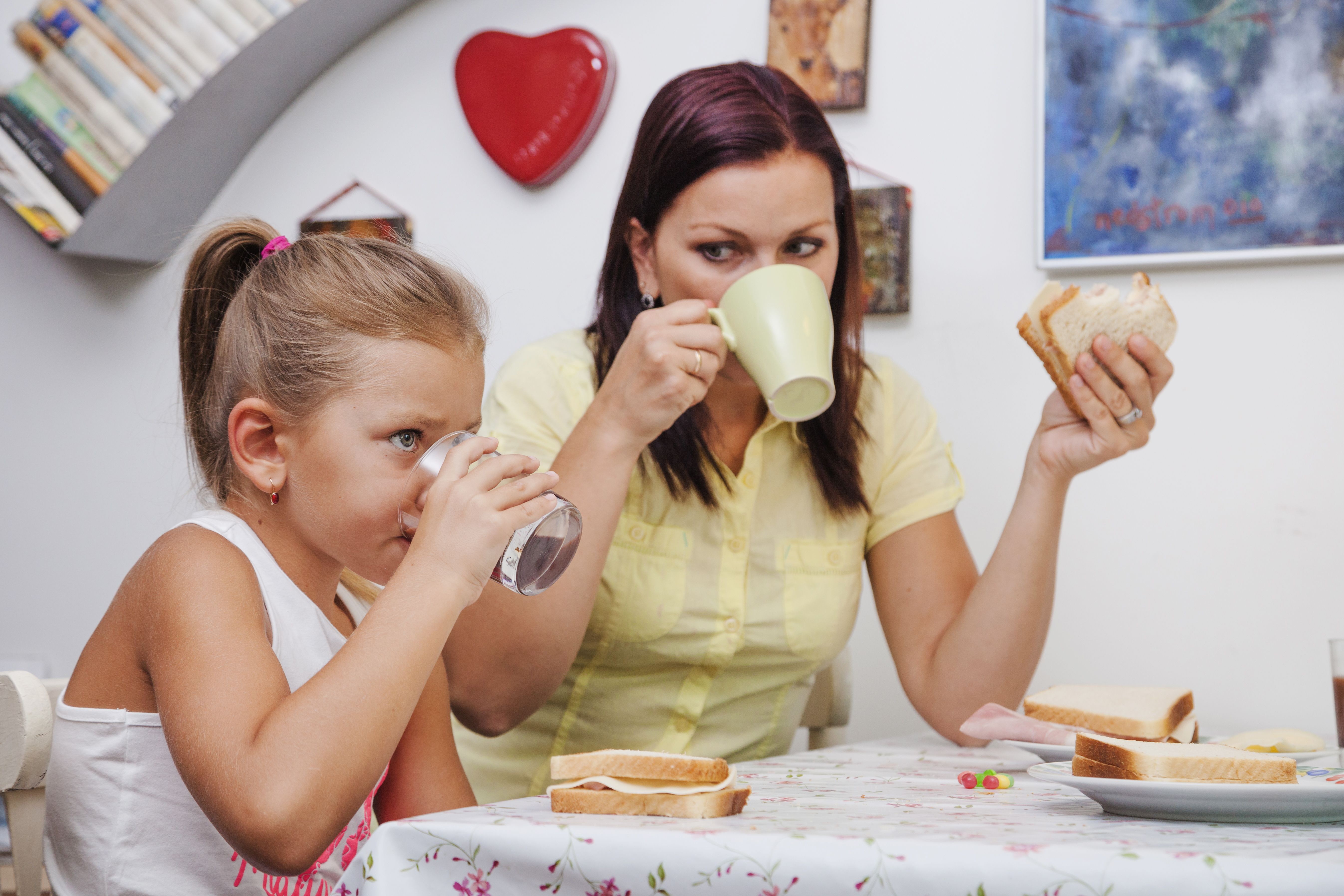 A female adult and young girl are eatting a sandwich and drinking water at a table.