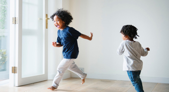 Two toddlers kids in a bright house setting playing chasing each other and laughing.