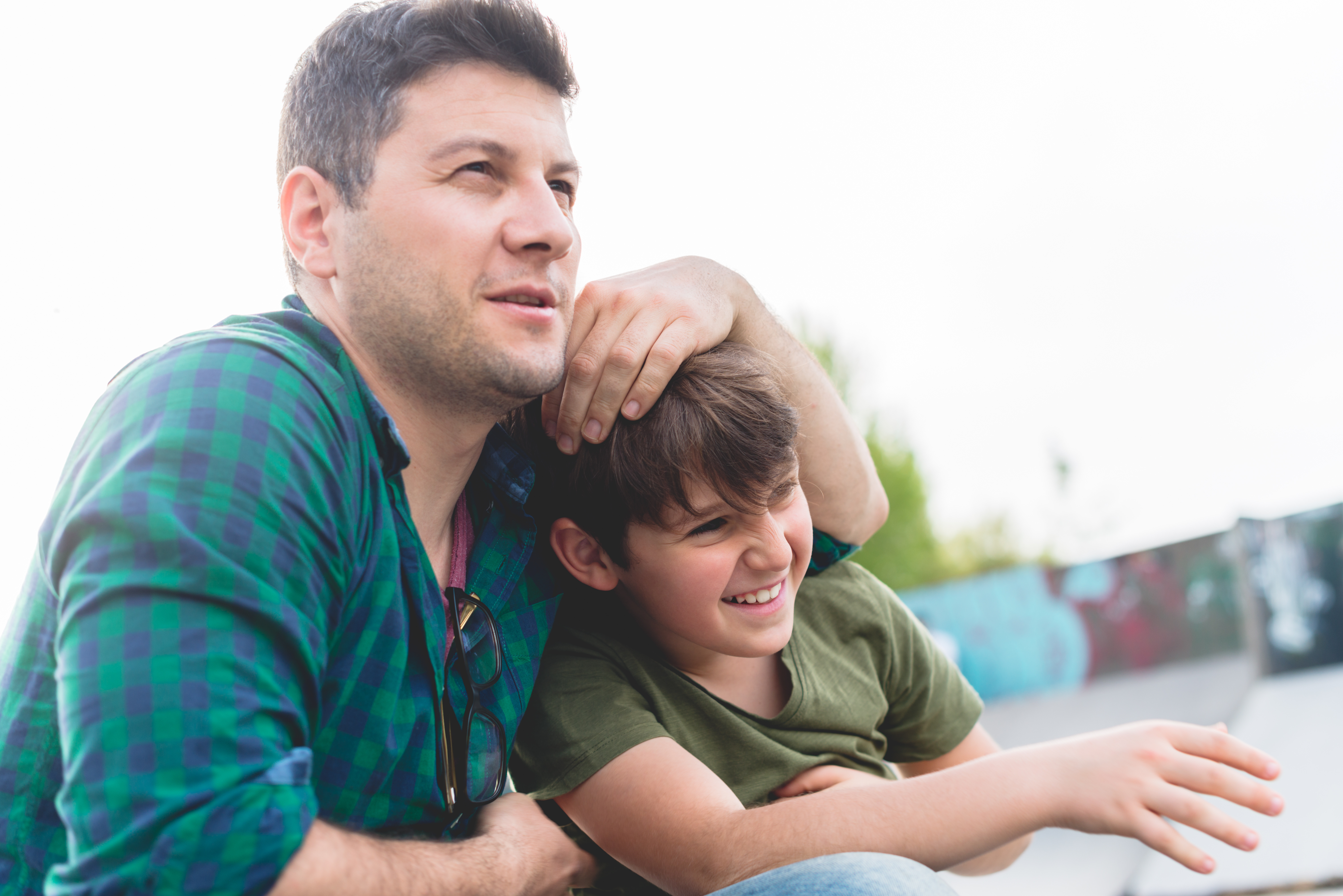 Adult male with young boy in outdoor setting. Both are looking off into the distance, smiling.