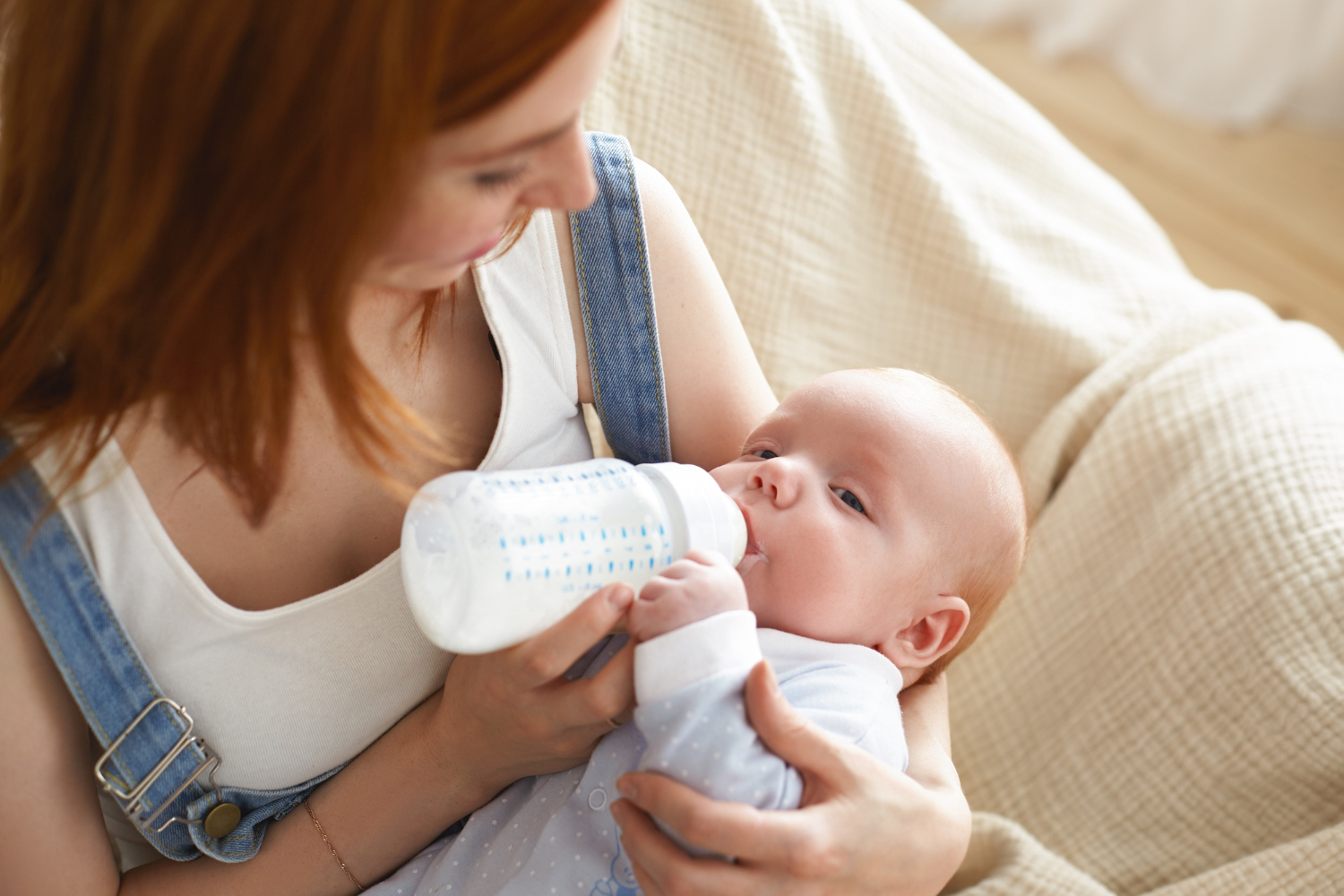 Adult female holding newborn and bottle feeding them. Cozy at home setting. 