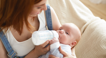 Adult female holding newborn and bottle feeding them. Cozy at home setting. 