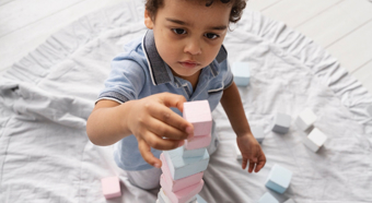 Closeup of toddler kid stacking little blocks in comfy at home setting.