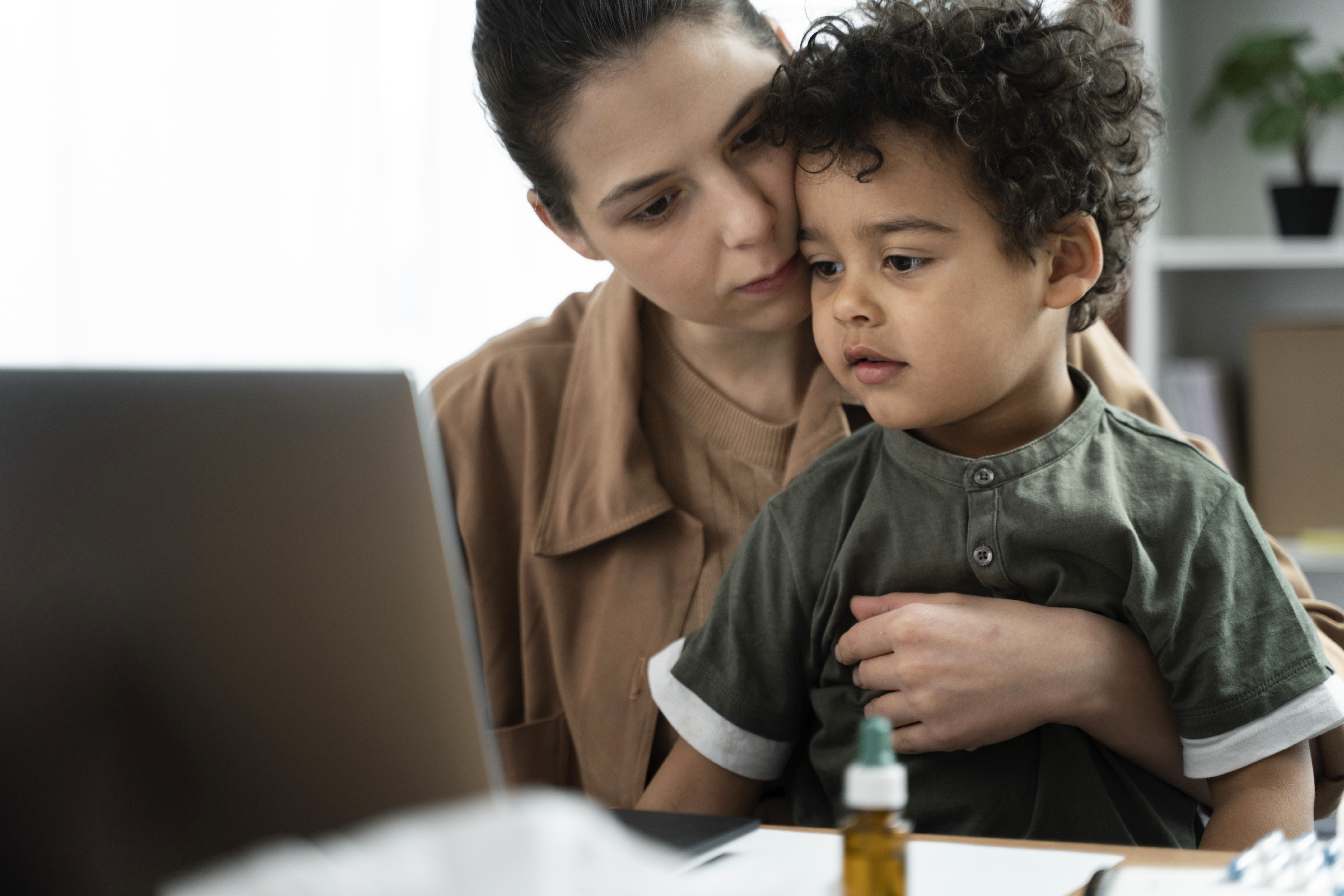 Women holding young boy in a dark green shirt on her lap, while both of them look at a laptop computer screen 