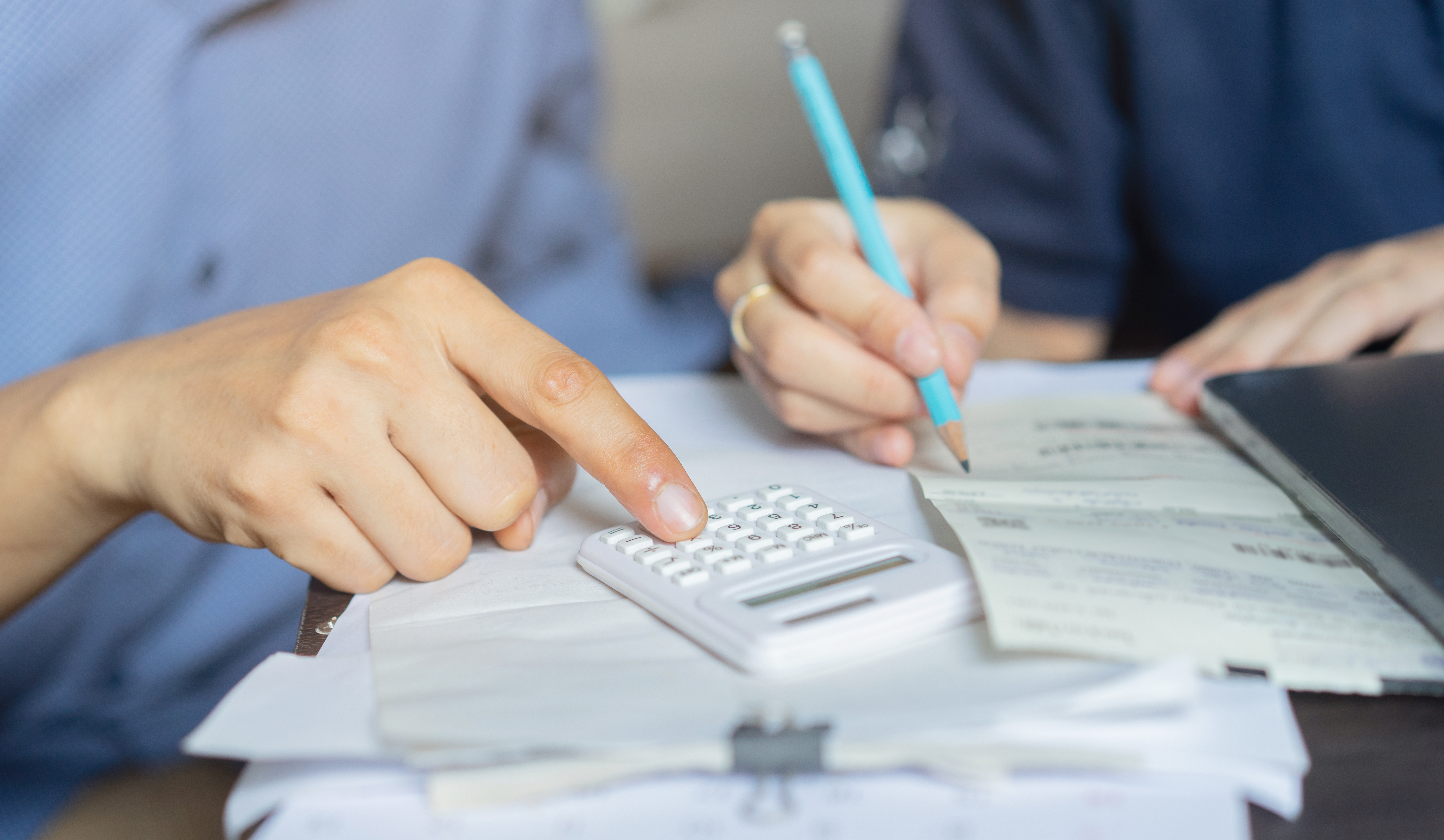 Picture of hands using a calculator and writing on a piece of paper.