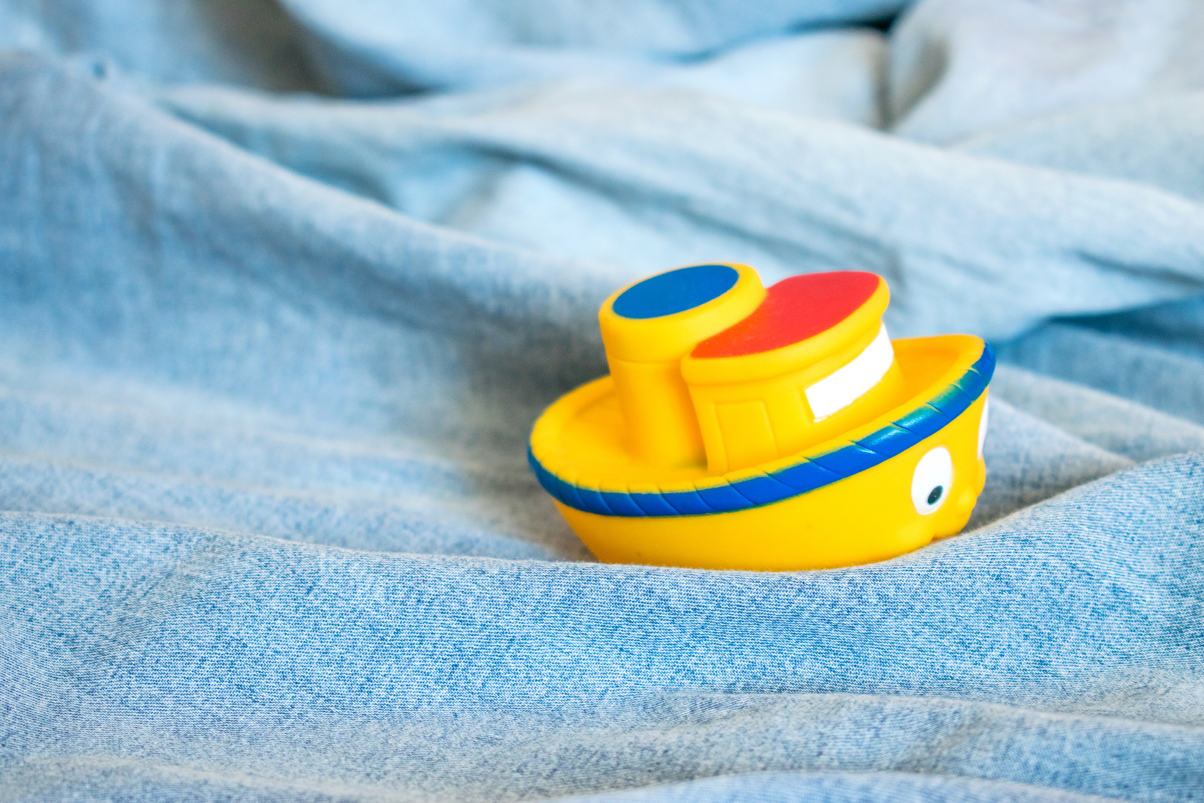 Little yellow toy boat sitting on light washed denim, looks like a little boat in water. 