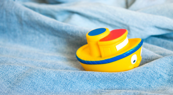 Little yellow toy boat sitting on light washed denim, looks like a little boat in water. 