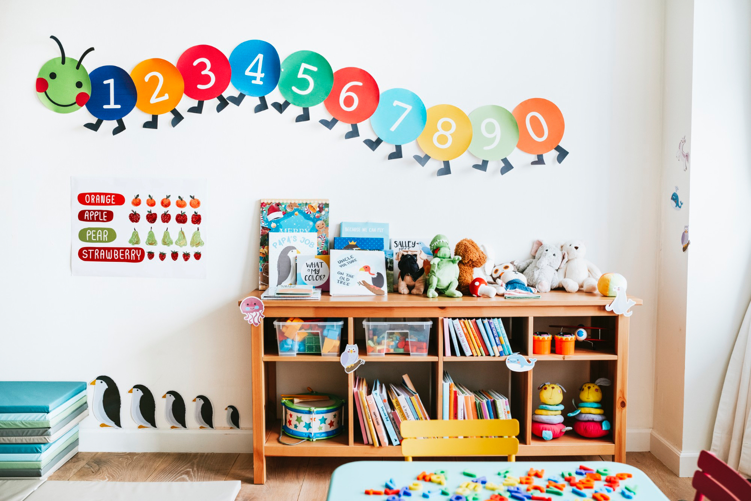 Inside a colorful kindergarten looking classroom, a bookshelf and colorful numbers on the wall. 