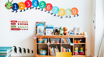 Inside a colorful kindergarten looking classroom, a bookshelf and colorful numbers on the wall. 